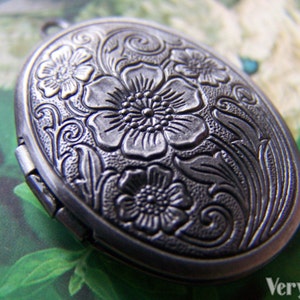 May include: Silver oval locket with an intricate floral design. The locket has a hinged opening and a detailed floral pattern.