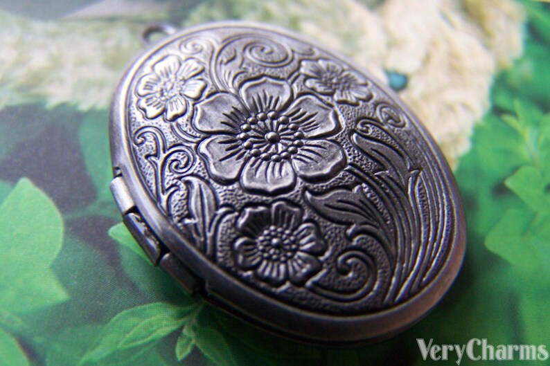 May include: Silver oval locket with an intricate floral design. The locket has a hinged opening and a detailed floral pattern.