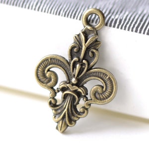 May include: Antique gold-toned metal charm featuring a detailed fleur-de-lis design. The charm has a loop at the top for attaching to jewelry or other crafts.