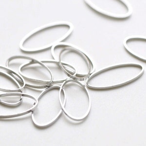 Può includere: Un gruppo di anelli ovali in metallo argentato, sparsi su una superficie bianca.