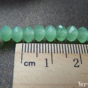 May include: A close-up of a strand of light green faceted beads, measured against a ruler. The beads are approximately 1 cm in diameter.