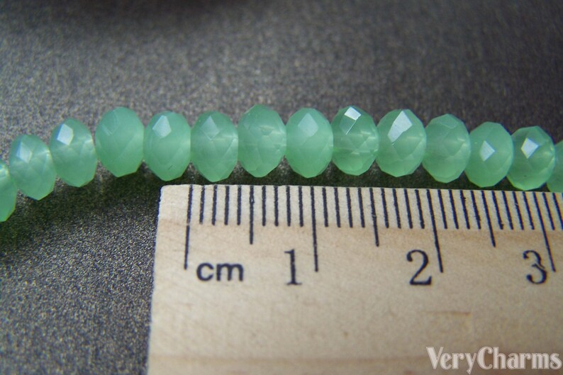 May include: A close-up of a strand of light green faceted beads, measured against a ruler. The beads are approximately 1 cm in diameter.