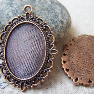May include: Two copper-coloured oval-shaped pendant trays with ornate filigree edges. The tray on the left has a smooth, slightly textured surface. The tray on the right has a textured surface with a criss-cross pattern.