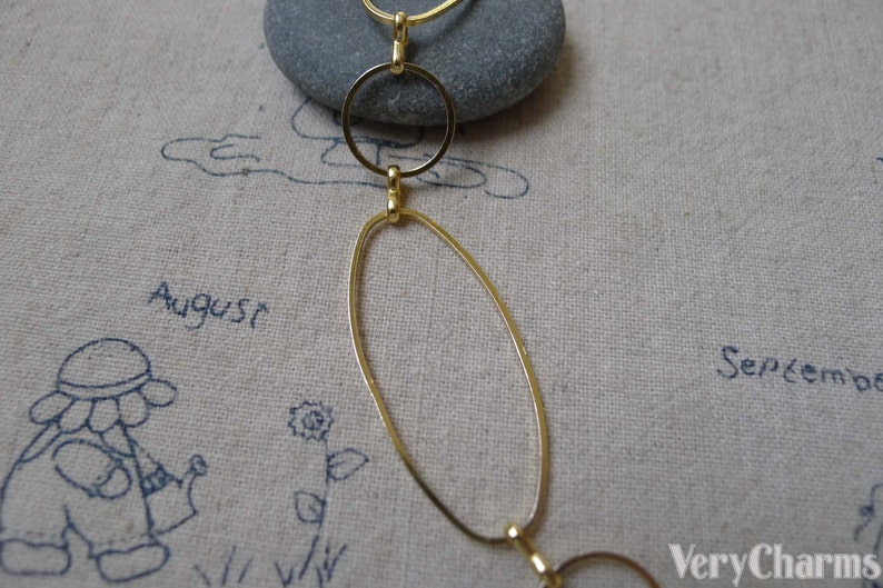 May include: Gold chain necklace with oval and round links. The chain is on a beige fabric background with the words "August" and "September" written on it.