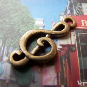 May include: A gold-colored metal charm shaped like a treble clef. The charm is a popular design for jewelry and is often used to represent music.