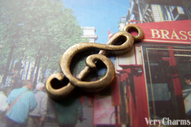 May include: A gold-colored metal charm shaped like a treble clef. The charm is a popular design for jewelry and is often used to represent music.