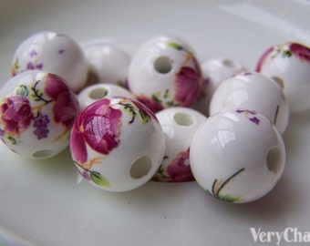 May include: A collection of white ceramic beads with a floral design. The beads are round and have a hole in the center. The flowers are pink and purple and have a white background.