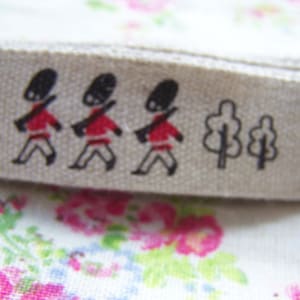 May include: White cotton ribbon with a black and red design of marching soldiers and trees. The ribbon has the text "London Traditions" printed on it.