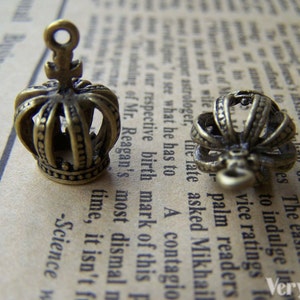 May include: Two antique gold-toned crown charms with a detailed design. The crowns have a pointed top and a loop for attaching to a necklace or bracelet.