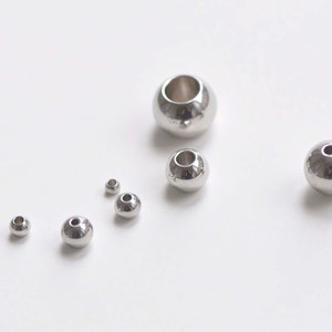 May include: A set of seven silver metal beads of varying sizes. The beads have a hole in the center for stringing.