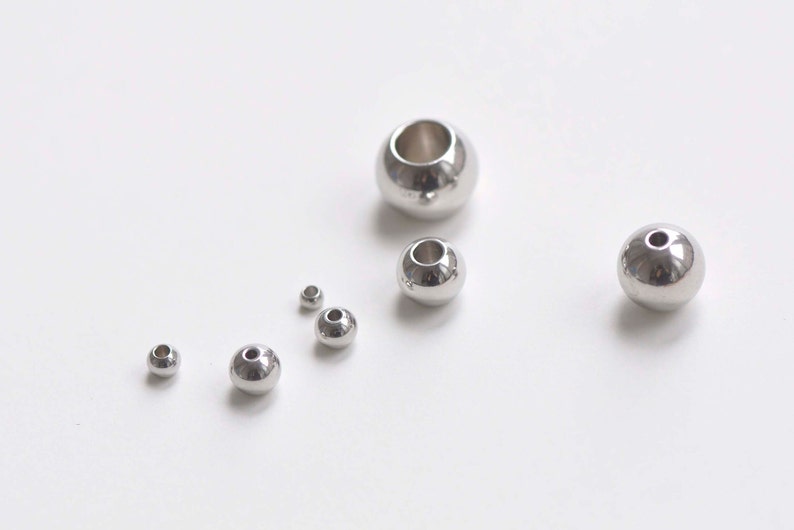May include: A set of seven silver metal beads of varying sizes. The beads have a hole in the center for stringing.