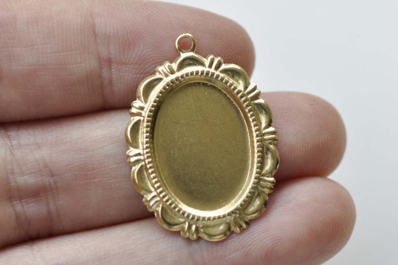 Peut inclure: Pendentif ovale en m&eacute;tal dor&eacute; avec un bord festonn&eacute;. Le pendentif a une surface lisse et plate, id&eacute;ale pour ajouter un motif ou une image.