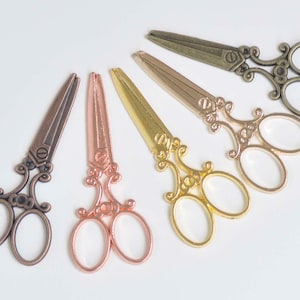May include: Five pairs of decorative scissors with ornate handles. The scissors are in various metallic finishes, including copper, bronze, gold, and rose gold.