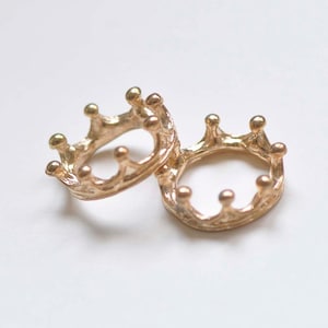 May include: Two gold-colored crown-shaped rings. The rings are interlocking and have a detailed design.