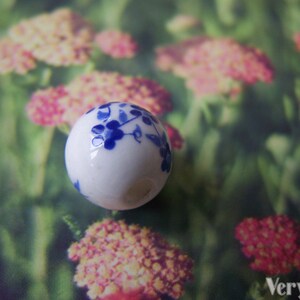 Puede incluir: Una bola de cer&aacute;mica blanca con un dise&ntilde;o floral azul. La bola tiene un di&aacute;metro de aproximadamente 2,5 cm.