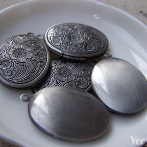 May include: Five silver oval-shaped locket charms with floral designs. Some of the lockets have a smooth finish, while others have an engraved floral pattern.