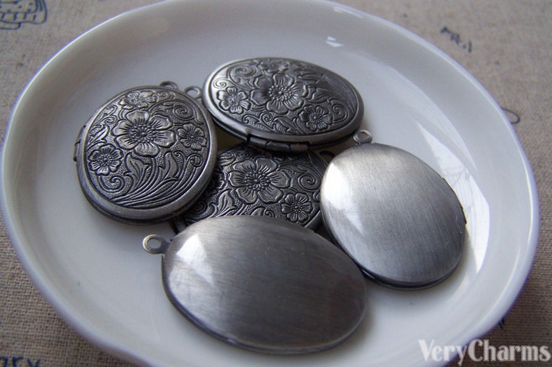 May include: Five silver oval-shaped locket charms with floral designs. Some of the lockets have a smooth finish, while others have an engraved floral pattern.