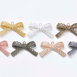 Könnte beinhalten: Acht Metall-Spitzen-Schleifen-Anhänger in verschiedenen Farben, darunter Gold, Silber, Bronze und Roségold. Die Schleifen sind zart und filigran, mit einer kleinen Schlaufe oben zum Anbringen an Schmuck oder anderen Bastelarbeiten.
