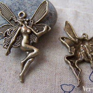 May include: Two antique gold-toned metal fairy charms with intricate details. One charm features a fairy with wings outstretched and the other charm features a fairy with wings folded.