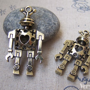May include: Two gold-toned metal robot charms with a heart-shaped cutout in the center of their bodies. The charms are detailed with intricate designs and have a vintage aesthetic.