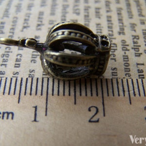 May include: A small, gold-colored crown charm with a single, clear rhinestone. The charm is about 1.5 cm long and is shown next to a ruler.