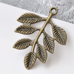 Peut inclure: Un charme en métal de couleur bronze en forme de branche feuillue avec cinq feuilles. Le charme a une boucle en haut pour l'attacher à des bijoux ou d'autres objets artisanaux.