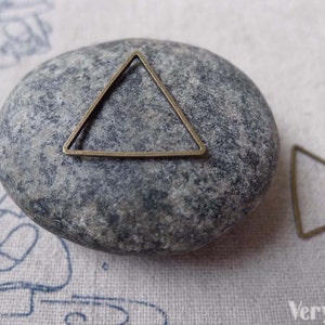May include: Two antique gold triangle shaped metal frames. The larger frame is on a gray rock. The smaller frame is on a white fabric surface. The text "VeryCharms" is visible in the bottom right corner of the image.