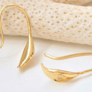 May include: A pair of gold-toned earrings with a leaf-shaped design. The earrings are made of a smooth, shiny metal and have a simple, elegant style.
