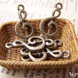 May include: A small wicker basket filled with antique silver treble clef charms. The charms are in various sizes and are arranged in a random pattern.