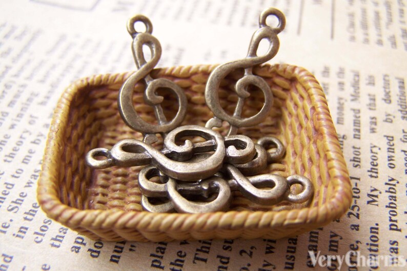 May include: A small wicker basket filled with antique silver treble clef charms. The charms are in various sizes and are arranged in a random pattern.