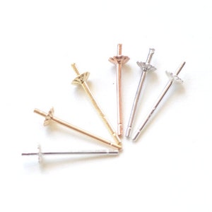 May include: Five earring posts with different colored metal finishes. The posts are made of silver, gold, and rose gold. The posts are designed to hold a pearl or other gemstone.