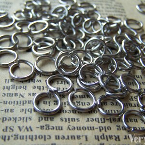 Może przedstawiać: Duża sterta srebrnych k&oacute;łek do łączenia, rodzaj metalowego pierścienia używanego w produkcji biżuterii.