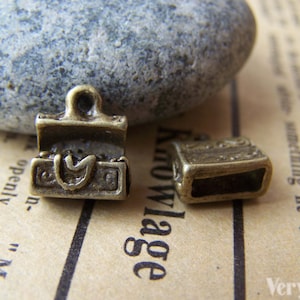 May include: Two antique gold-toned metal charms shaped like small treasure chests. One charm is open and the other is closed.