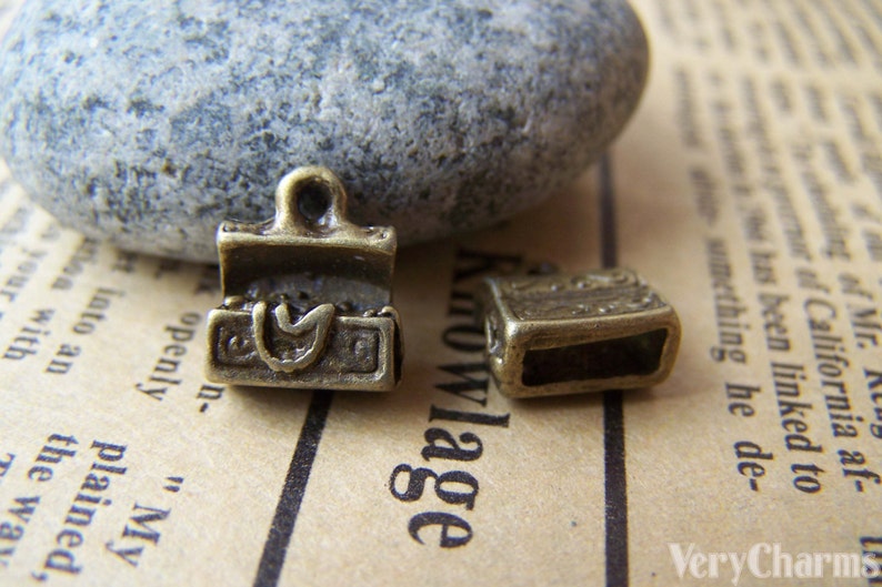 May include: Two antique gold-toned metal charms shaped like small treasure chests. One charm is open and the other is closed.