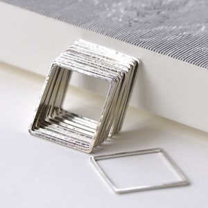 May include: A stack of silver square rings with a textured finish. The rings are arranged in a diamond shape and are on a white surface.