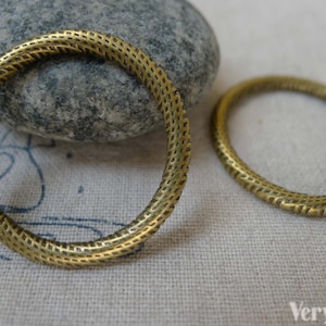 Puede incluir: Dos anillos de metal de color dorado con una superficie texturizada. Los anillos tienen un diámetro de aproximadamente 5 cm.