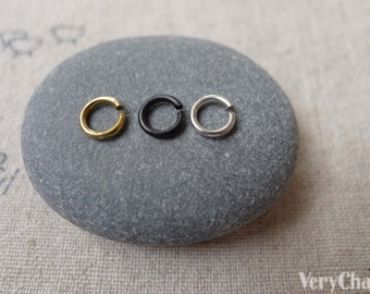 May include: Three jump rings in gold, black, and silver, displayed on a gray stone.