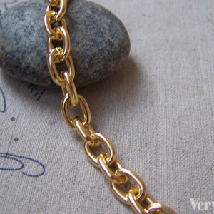 May include: Gold chain link with a smooth, polished finish. The chain is lying on a textured fabric surface.
