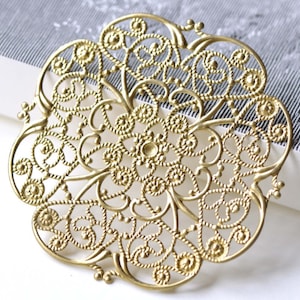 May include: A gold filigree design with a circular shape and intricate details. The design is made of thin, twisted wire and has a delicate, airy feel.