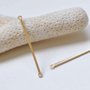 May include: Two gold metal connector bars with loops at each end. The bars are straight and have a smooth finish.