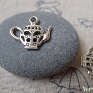 May include: Two silver teapot charms with an intricate design. The charms are made of metal and have a detailed, cutout pattern. They are perfect for adding a touch of whimsy to jewelry or crafts.