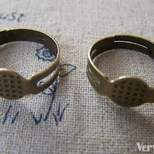 May include: Two antique gold-toned metal rings with a textured circular design. The rings have a split opening for attaching charms or other jewelry.