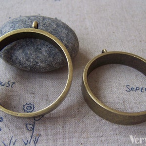 May include: Two antique gold metal hoops with a jump ring at the top. The hoops are different sizes.