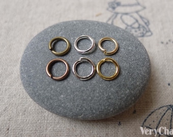 Puede incluir: Seis anillos de salto en diferentes acabados: oro, plata y bronce. Los anillos están dispuestos en dos filas de tres sobre una piedra gris.