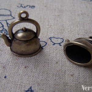 May include: Two antique gold-toned metal teapot charms. The teapot on the left has a handle and spout. The teapot on the right is missing the handle and spout.