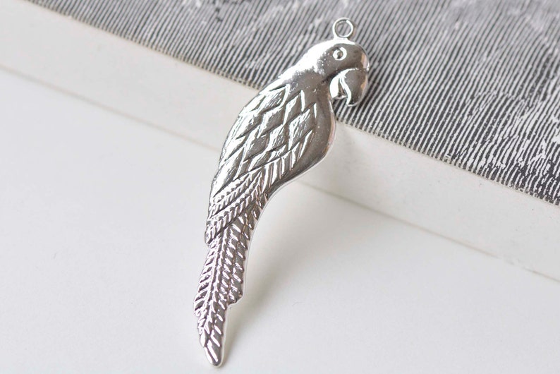 May include: Silver parrot charm with detailed feather design. The charm has a loop at the top for attaching to jewelry.