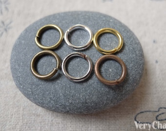 Puede incluir: Seis anillos de salto en diferentes acabados: oro, plata y bronce. Los anillos están dispuestos en dos filas de tres sobre una piedra gris.