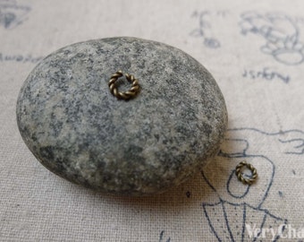 May include: Two small, gold-colored, twisted metal rings on a gray rock. The rings are about 1/2 inch in diameter.