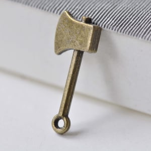 May include: A small, antique gold-toned metal axe charm with a loop at the bottom for attaching to a necklace or bracelet.