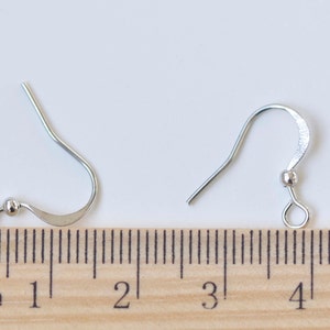 May include: Two silver earring hooks with a small ball at the top of the hook. The hooks are measured against a ruler, showing they are approximately 2 cm long.